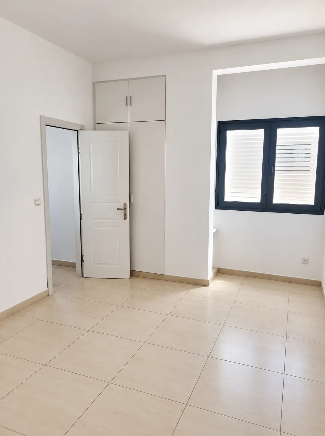 Chambre nue, fenêtre à châssis noir et jalousies